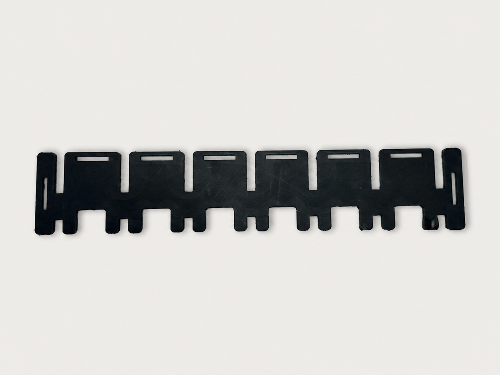 Long black HDPE strip with a repeating stepped tab profile and narrow rectangular slots